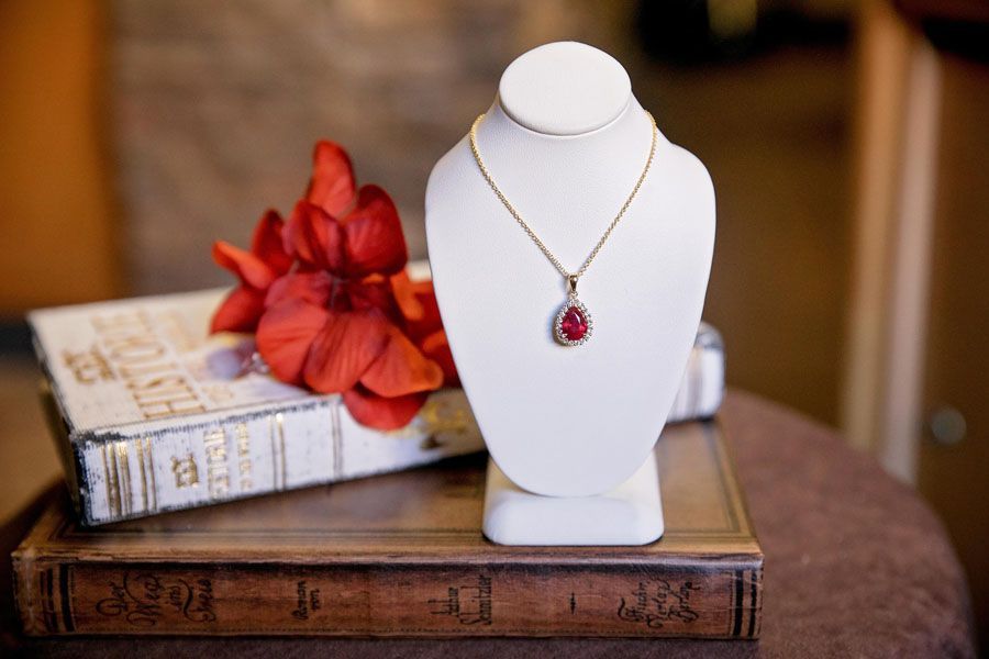 White necklace bust with red pendant on a wooden box, beside wrapped gifts and red ribbon