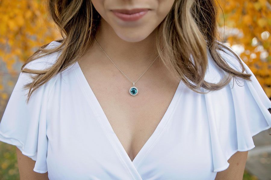 Woman wearing a white V-neck dress and turquoise pendant necklace against an autumn background