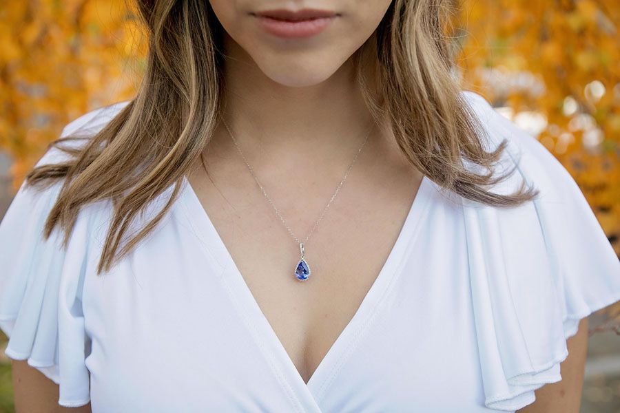 Close-up of a woman in a white dress wearing a blue pendant necklace, with autumn leaves blurred behind her