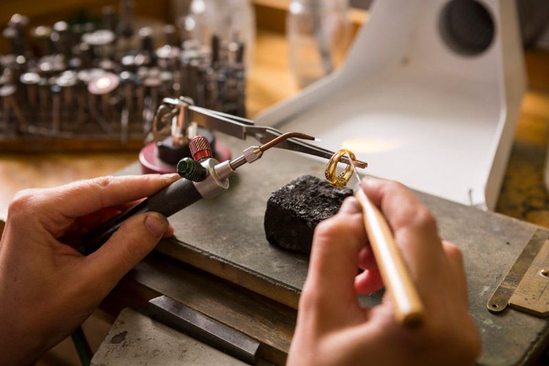Hands shaping a ring on a jewelry workbench with tools and a black stone block
