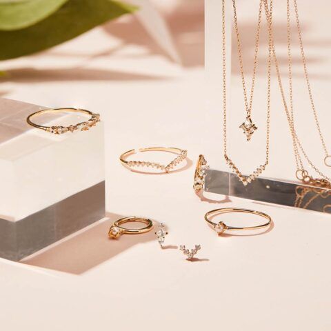 Gold rings and necklaces arranged on a pale display surface with soft beige lighting