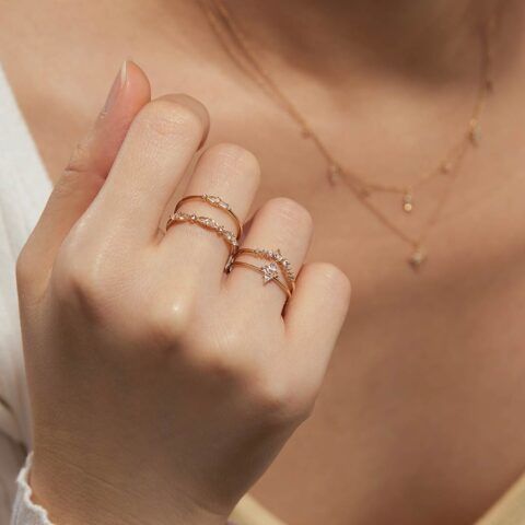 Hand with gold rings and delicate necklace against a soft beige background