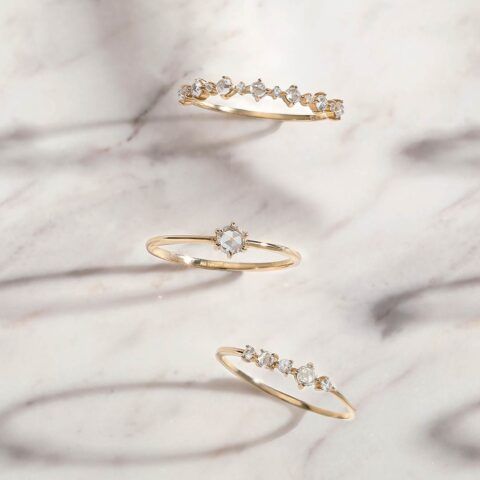 Three delicate gold rings with small diamonds on a white marble background