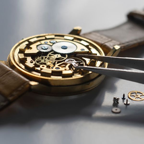 Close-up of a gold watch movement being repaired with tweezers on a brown leather strap