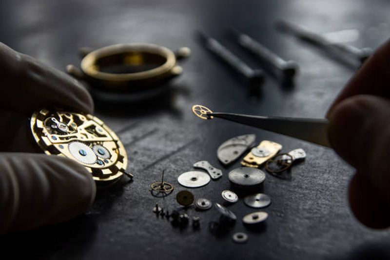 Watchmaker assembling tiny watch parts on a workbench with tools and a gold watch case