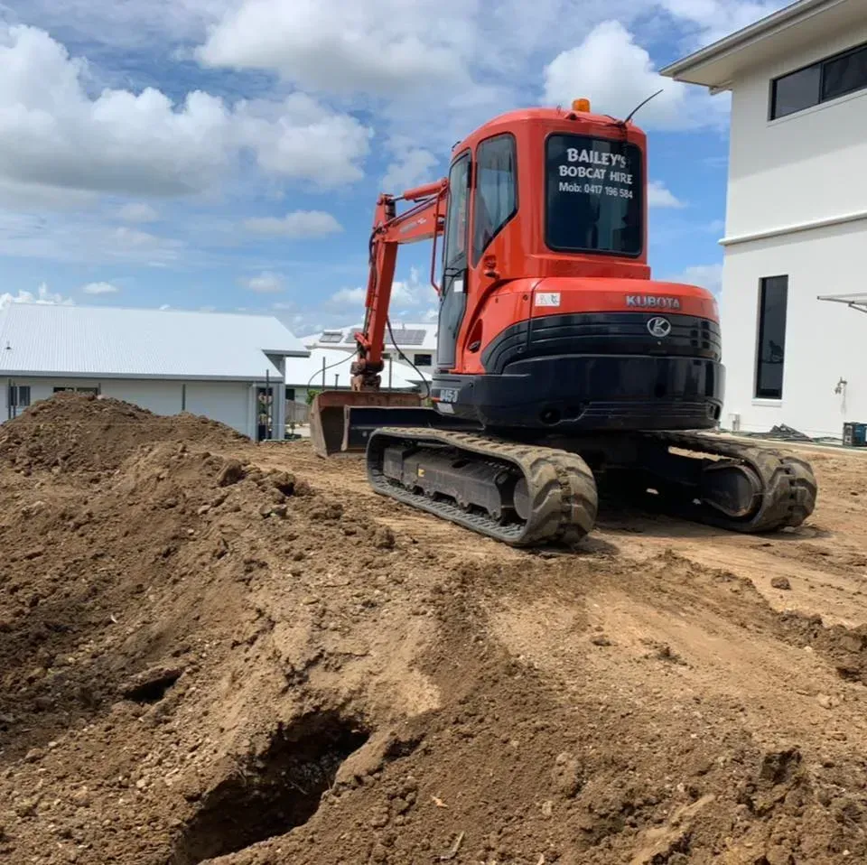 Orange Excavator on A Construction Site, with Dirt Piles and A White House in The Background — Bailey's Bobcat & Excavator Hire In Dumbleton, QLD