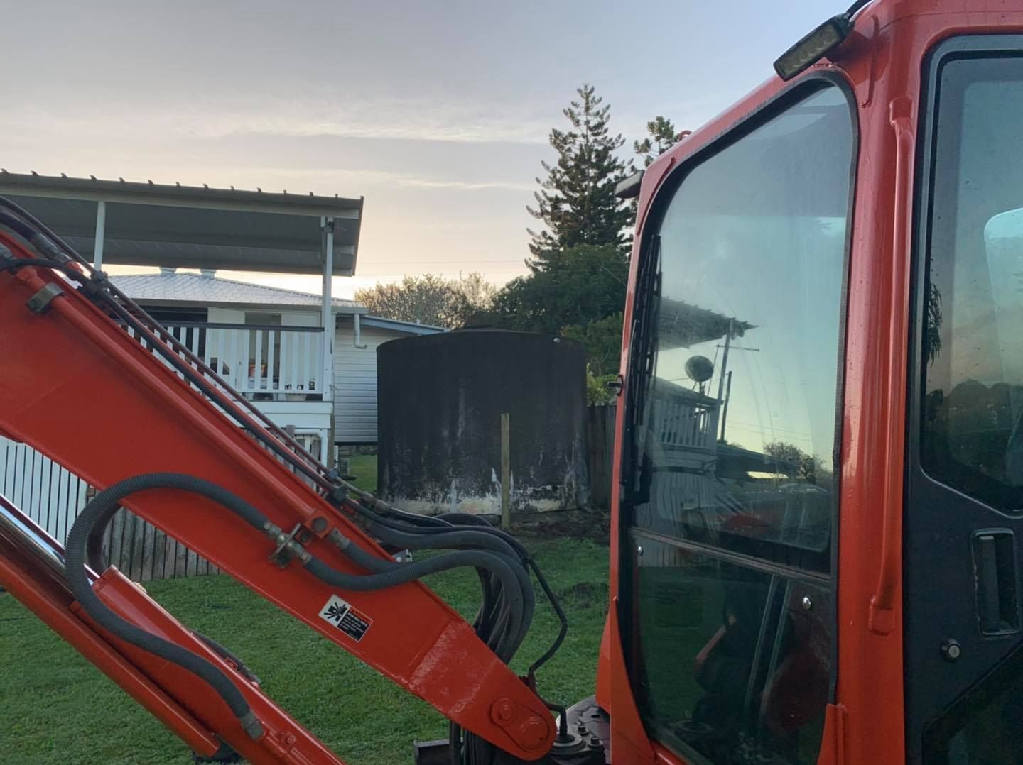 Orange Excavator Cab with A Glimpse of A House and Fuel Tank in The Background — Bailey's Bobcat & Excavator Hire In Dumbleton, QLD