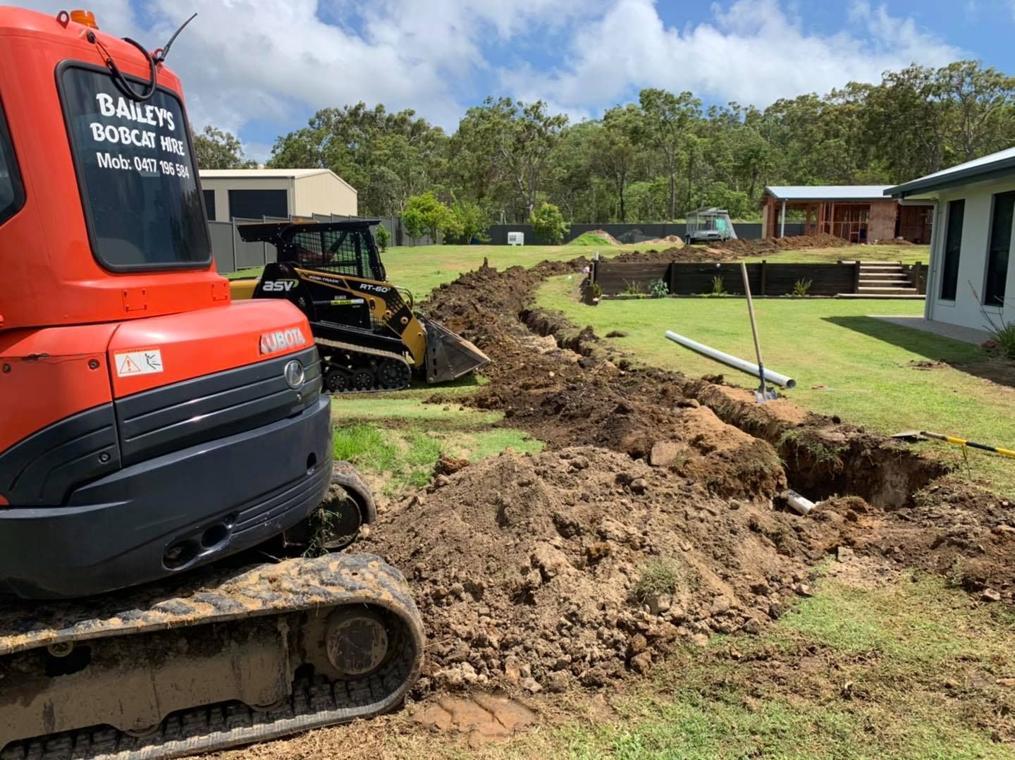 Orange Excavator and Small Bulldozer Digging Trench in A Yard Near a Building, Under a Sunny Sky — Bailey's Bobcat & Excavator Hire In Dumbleton, QLD