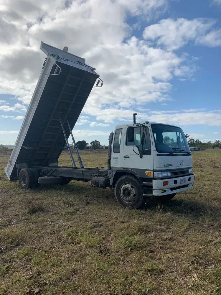 White Dump Truck with Raised Bed in A Grassy Field Under a Cloudy Sky — Bailey's Bobcat & Excavator Hire In Dumbleton, QLD