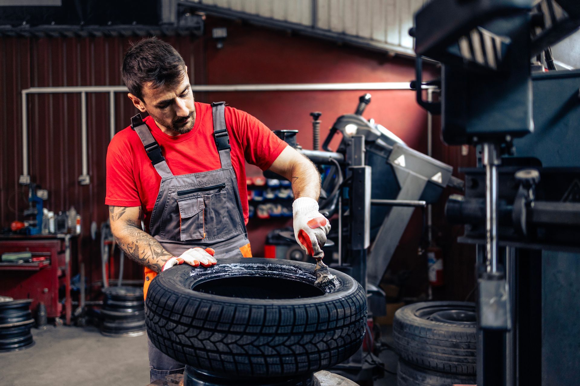 Mechanic in red shirt inspecting a tire in an auto workshop Mechanic in red shirt inspecting a tire in an auto workshop