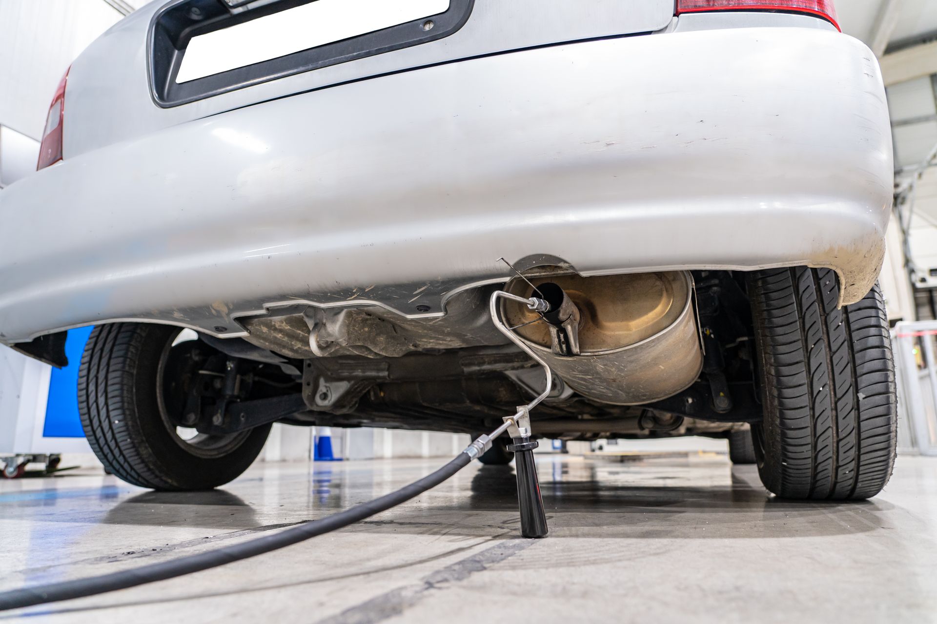 Rear view of a white car lifted on a jack in a garage, showing the undercarriage and rear wheel. Rear view of a white car lifted on a jack in a garage, showing the undercarriage and rear wheel.