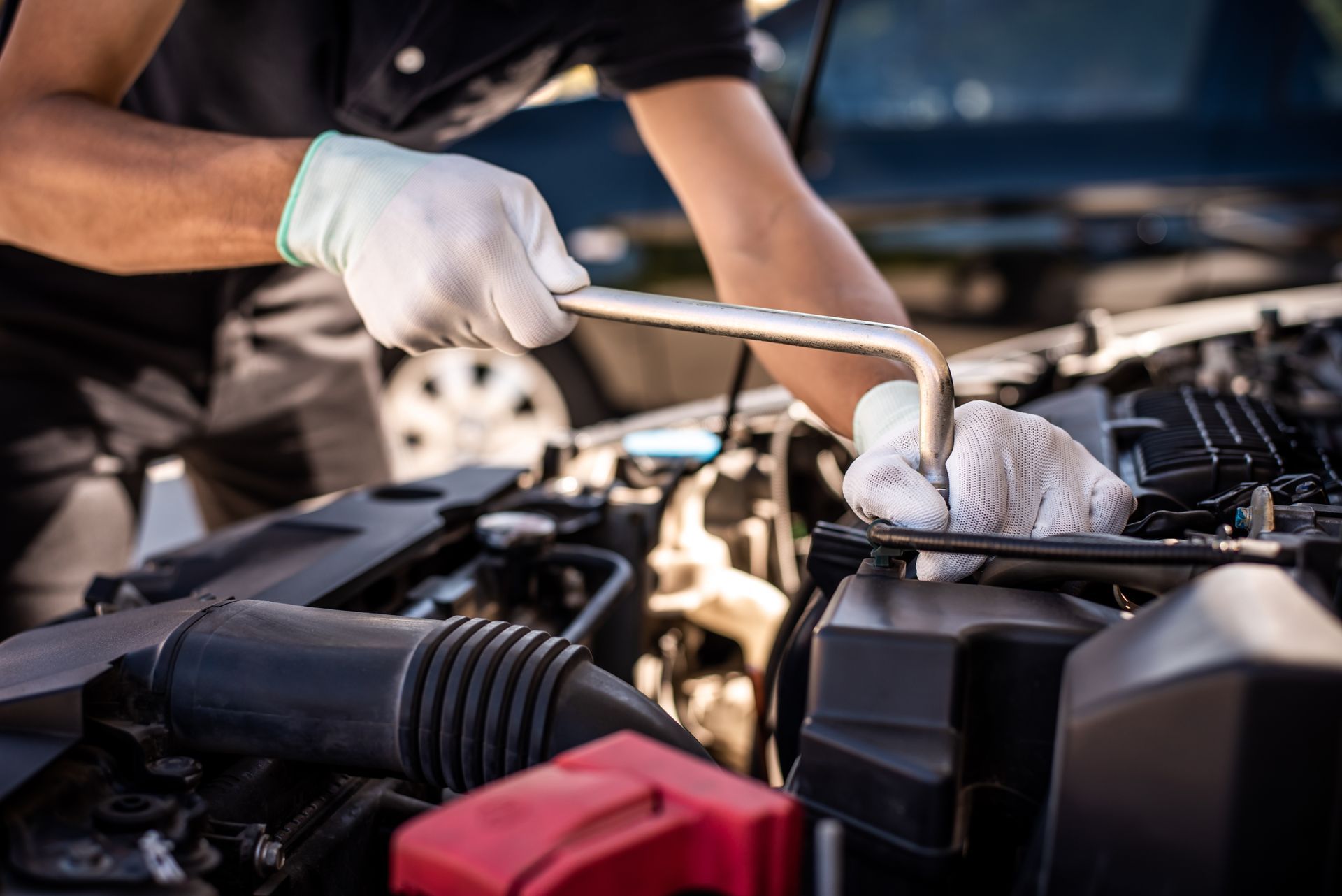 Gloved mechanic tightening a car engine part with a wrench under the hood Gloved mechanic tightening a car engine part with a wrench under the hood