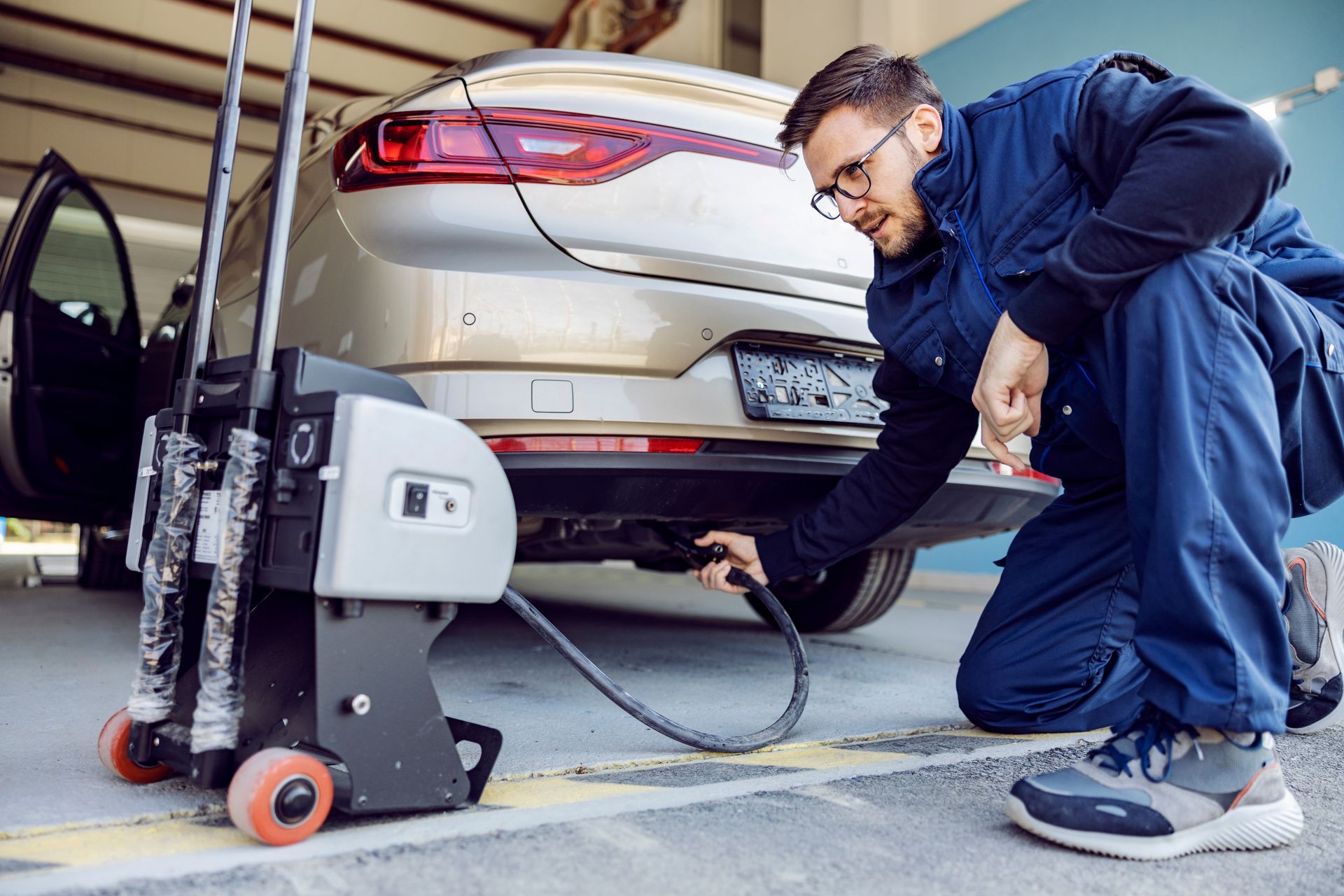 Mechanic inspecting the rear of a white car with a floor jack in a garage Mechanic inspecting the rear of a white car with a floor jack in a garage