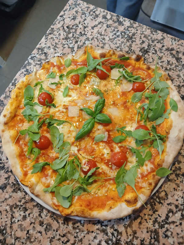 Una pizza appena sfornata con pomodorini, basilico e formaggio fuso su un piano di lavoro