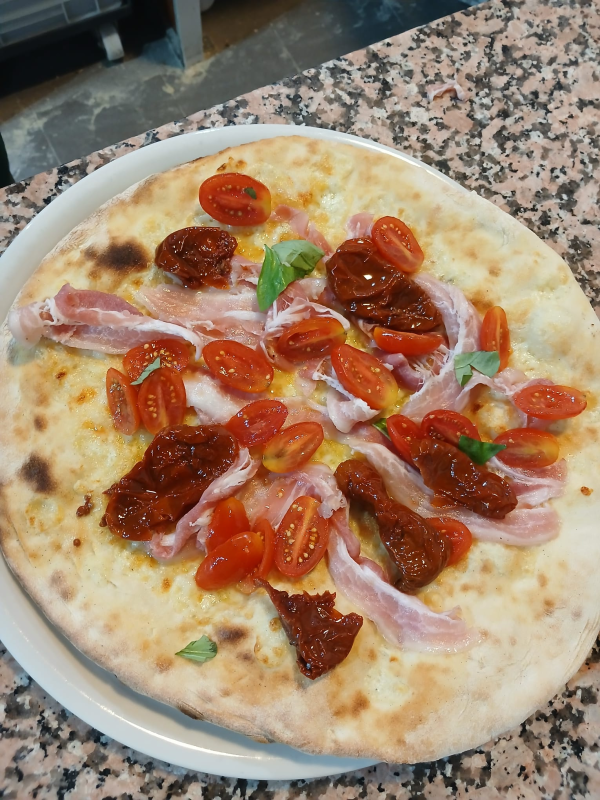 Una pizza condita con pomodorini, salame piccante, prosciutto crudo e cipolle rosse su un piatto bianco.
