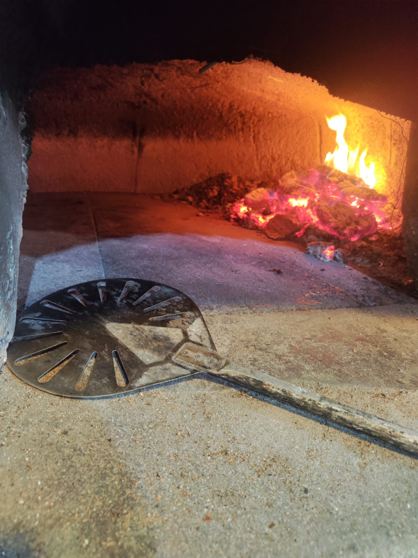 Detriti in fiamme in una nicchia buia, con una padella di metallo e un lungo manico sul pavimento di fronte.