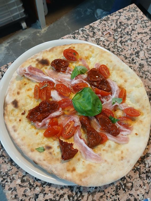 Piccola pizza condita con basilico, pomodorini, salumi e pomodori secchi, servita su un piatto.