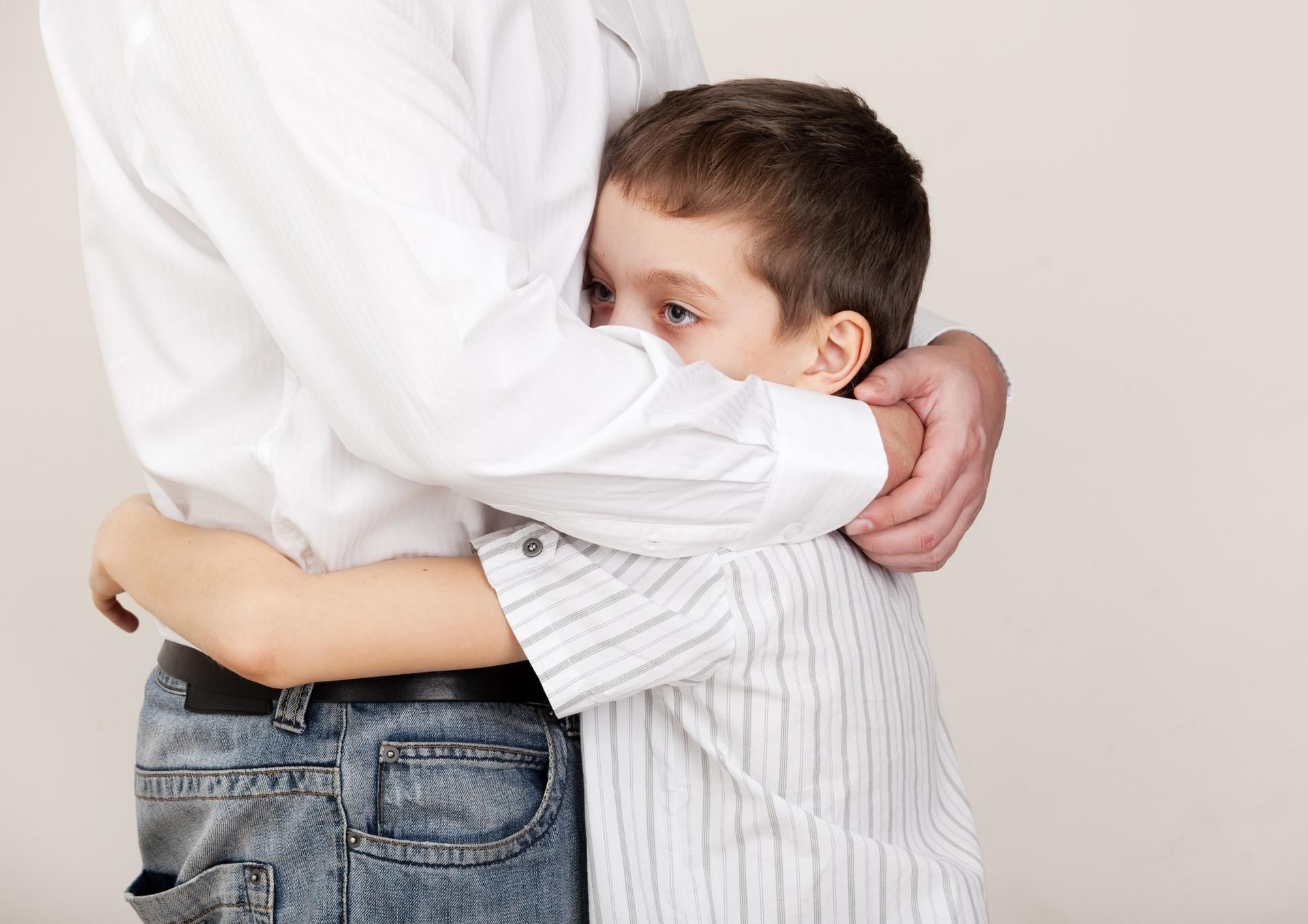 A man in jeans and a white shirt hugs a child, both against a white background.