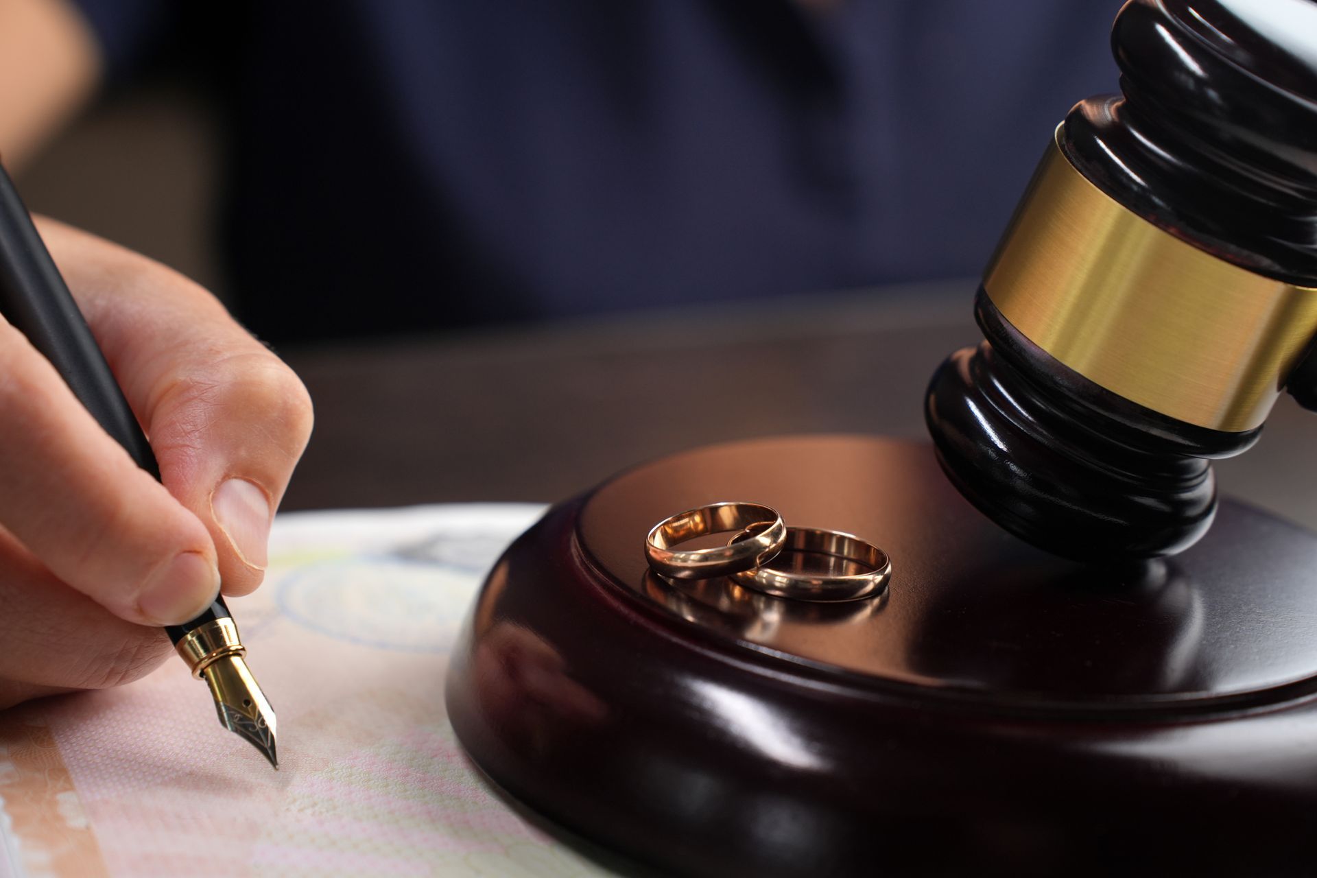 Close-up of a person signing a divorce document next to a gavel and wedding rings. Close-up of a person signing a divorce document next to a gavel and wedding rings.