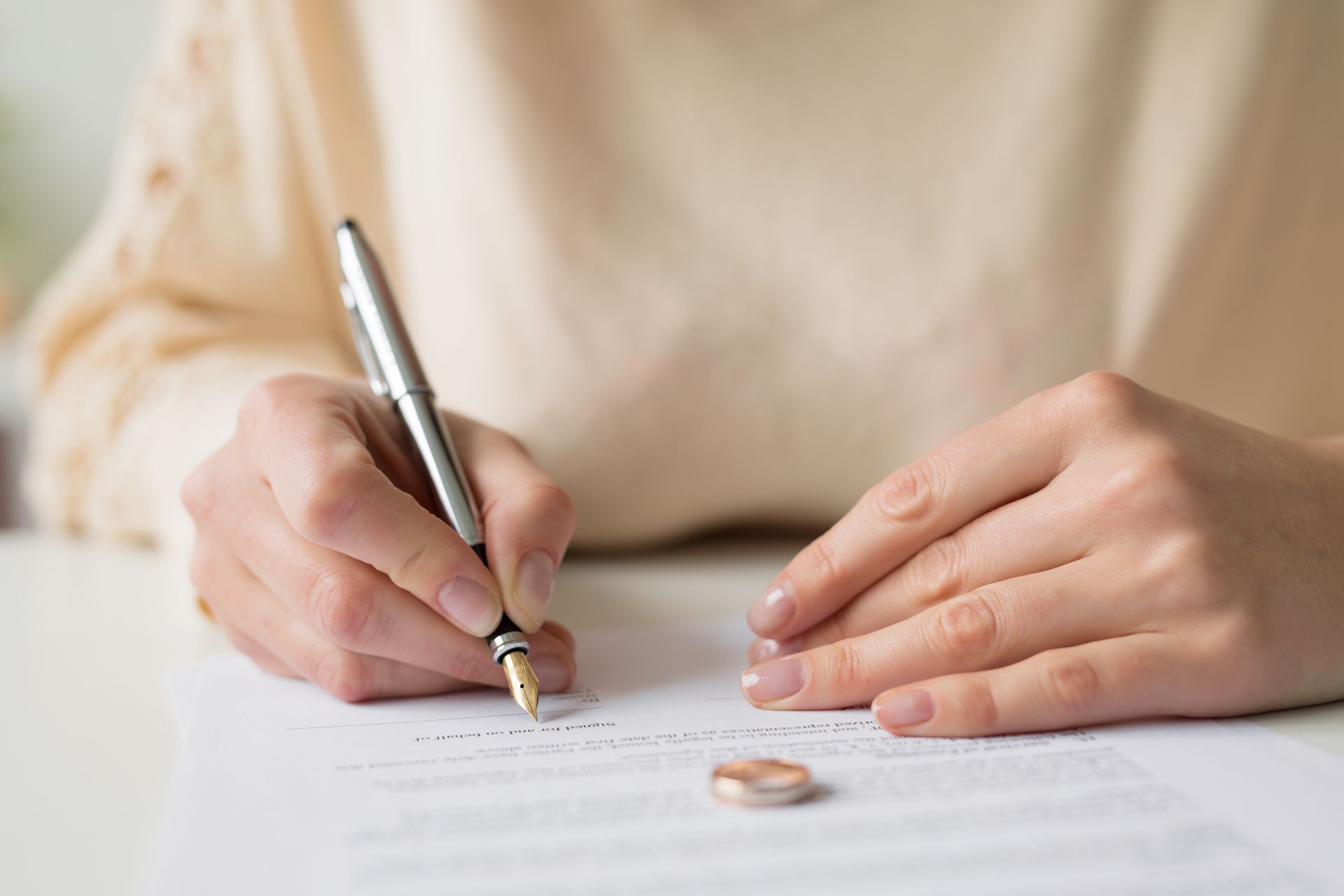Person signing legal documents with a wedding ring placed on the table.