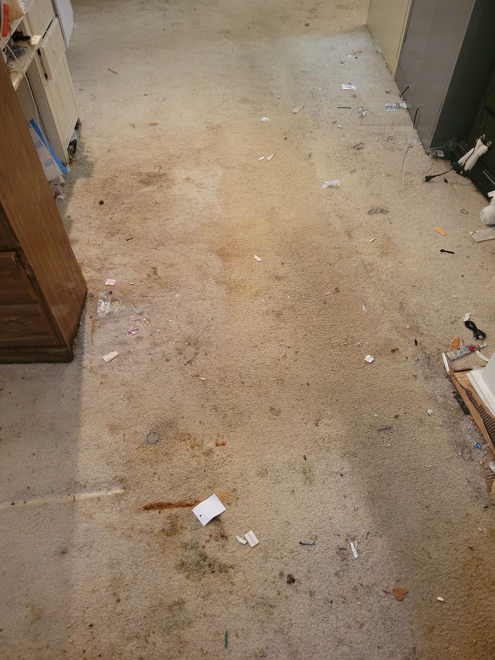 A dirty carpeted floor in a room with a dresser.