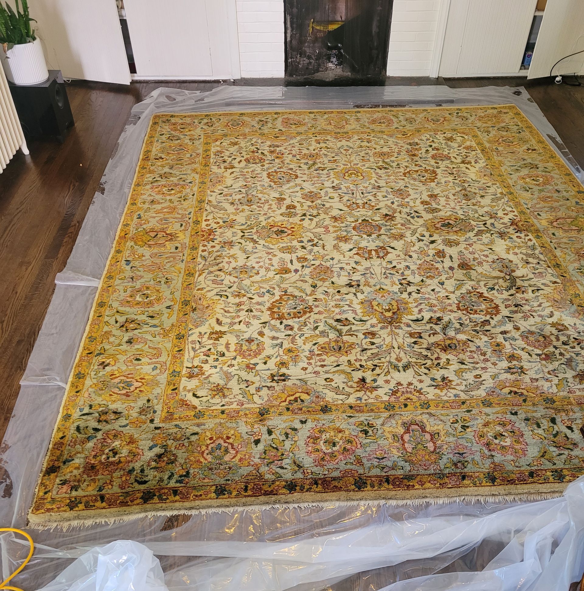 A large rug is sitting on a plastic sheet in a living room.