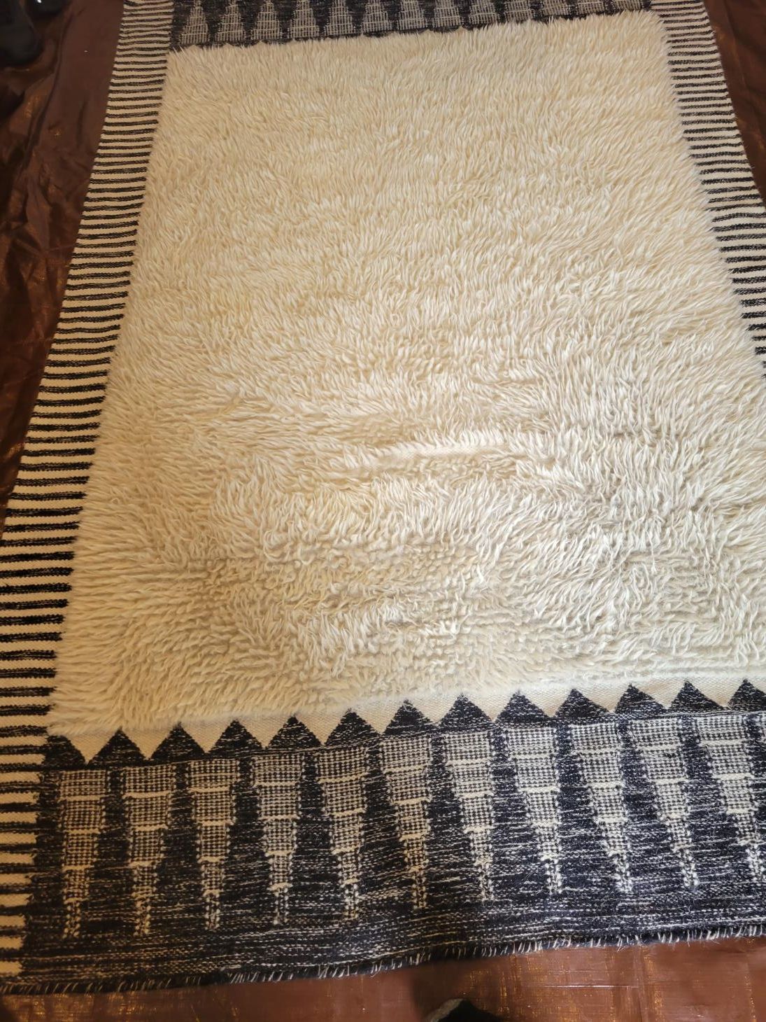 A white rug with a black border sits on a bed
