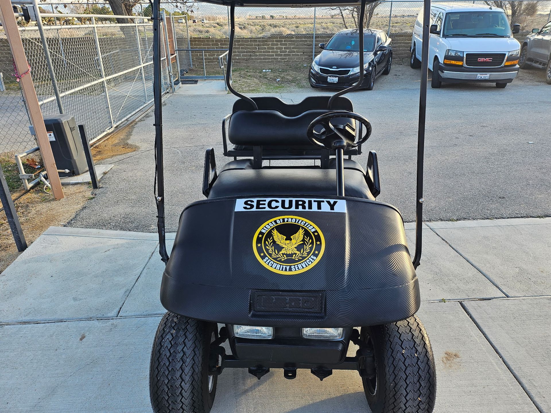 Black security golf cart parked outdoors on a driveway, with a yellow security badge on the front.