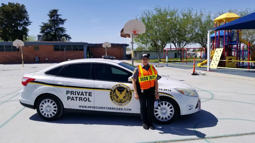 Private patrol car with officer standing beside it in a parking lot near a playground.