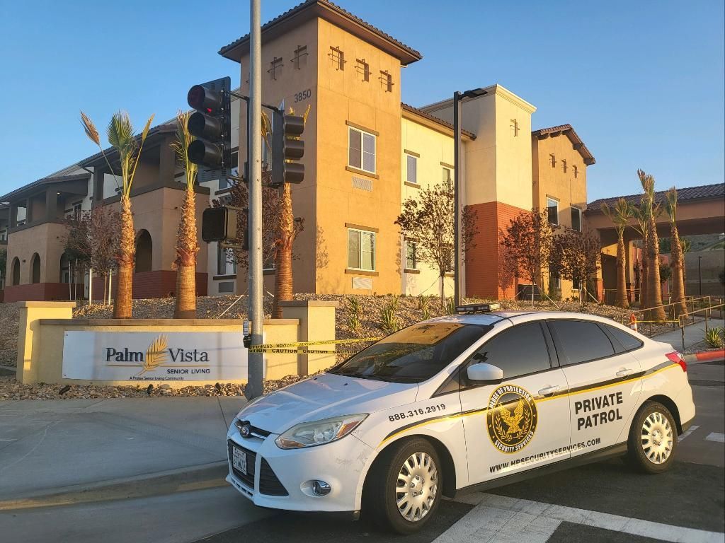 White security patrol car parked outside a tan apartment building at sunset