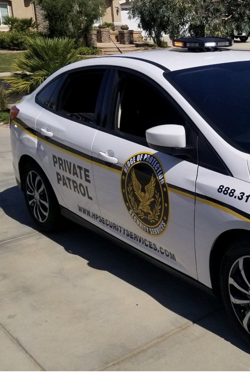 White private patrol car parked on a driveway, with gold lettering and a roof light bar.