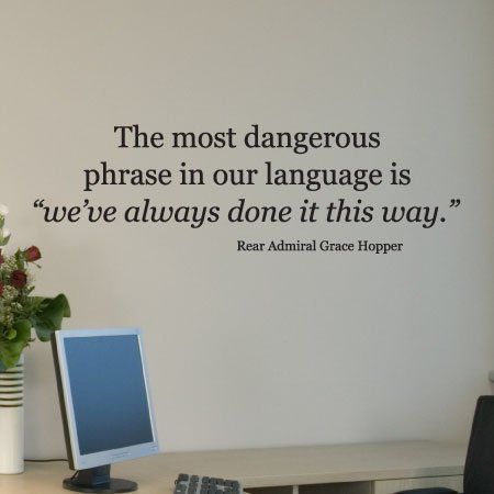 Wall decal quote above a desk: “we’ve always done it this way.” with a computer and flowers.
