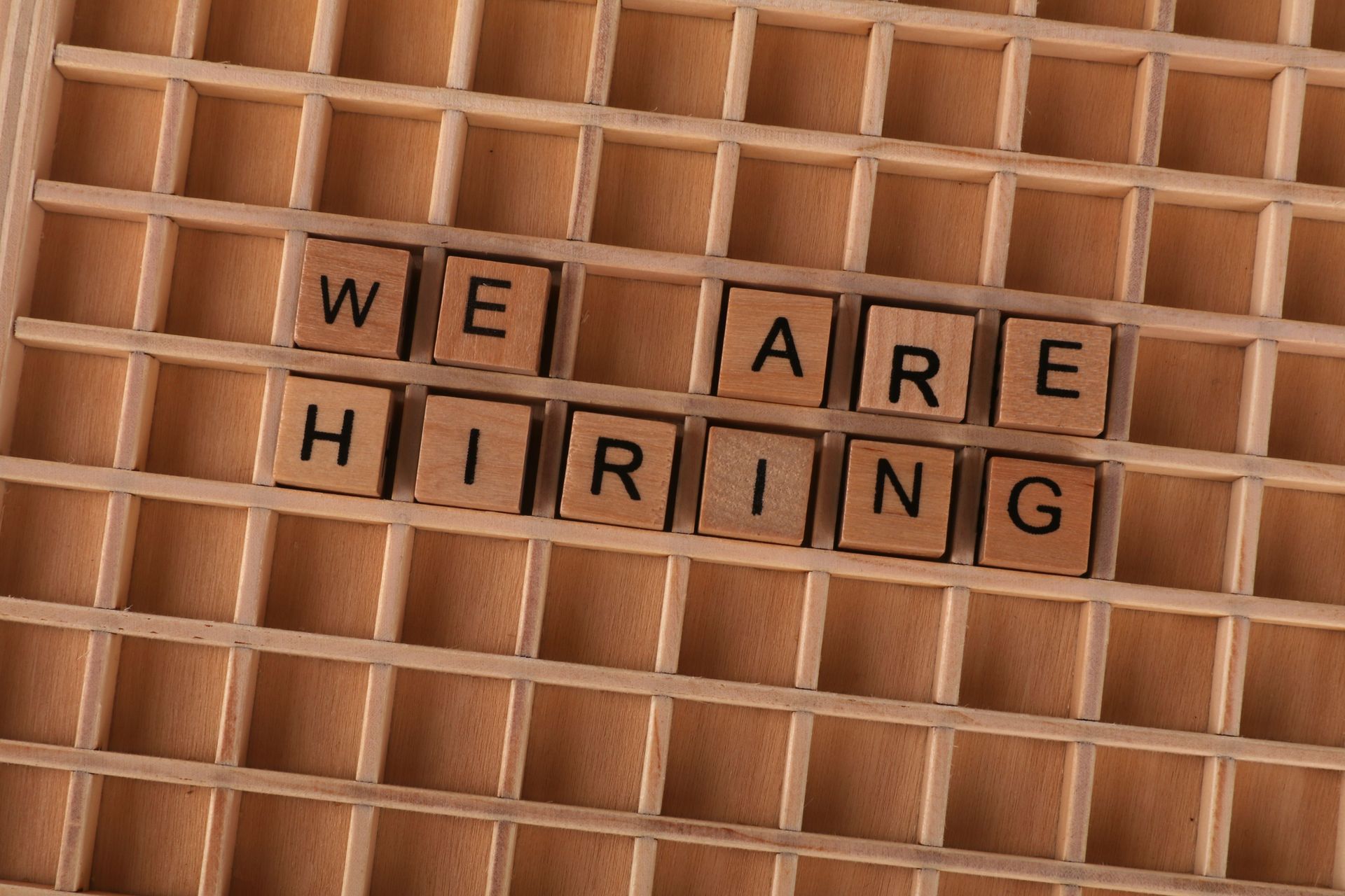 Teal “We’re Hiring!” text on a white background with brush-stroke lines