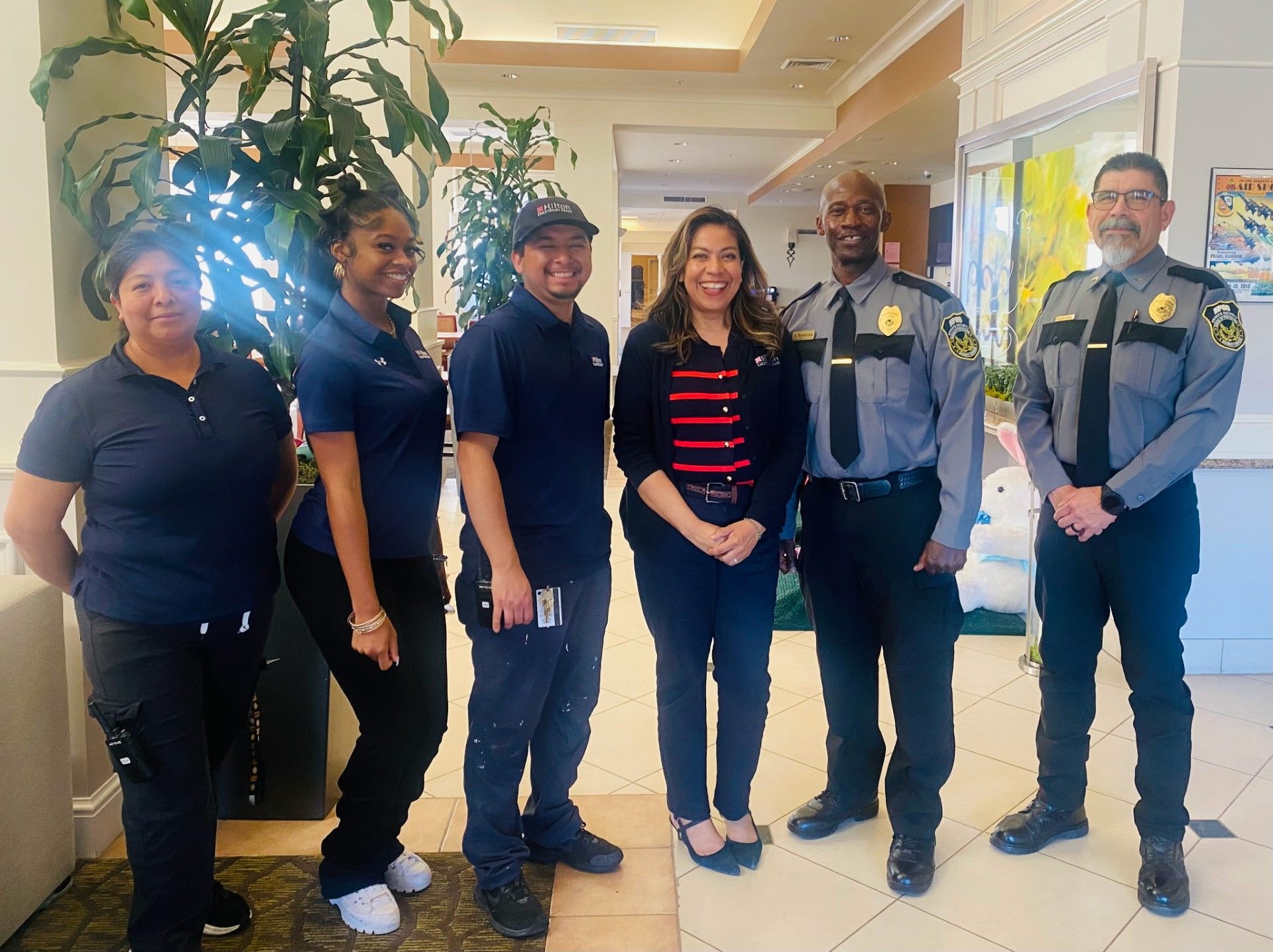 Six people posing together in a bright hallway, including two uniformed security officers and a woman in a striped shirt.