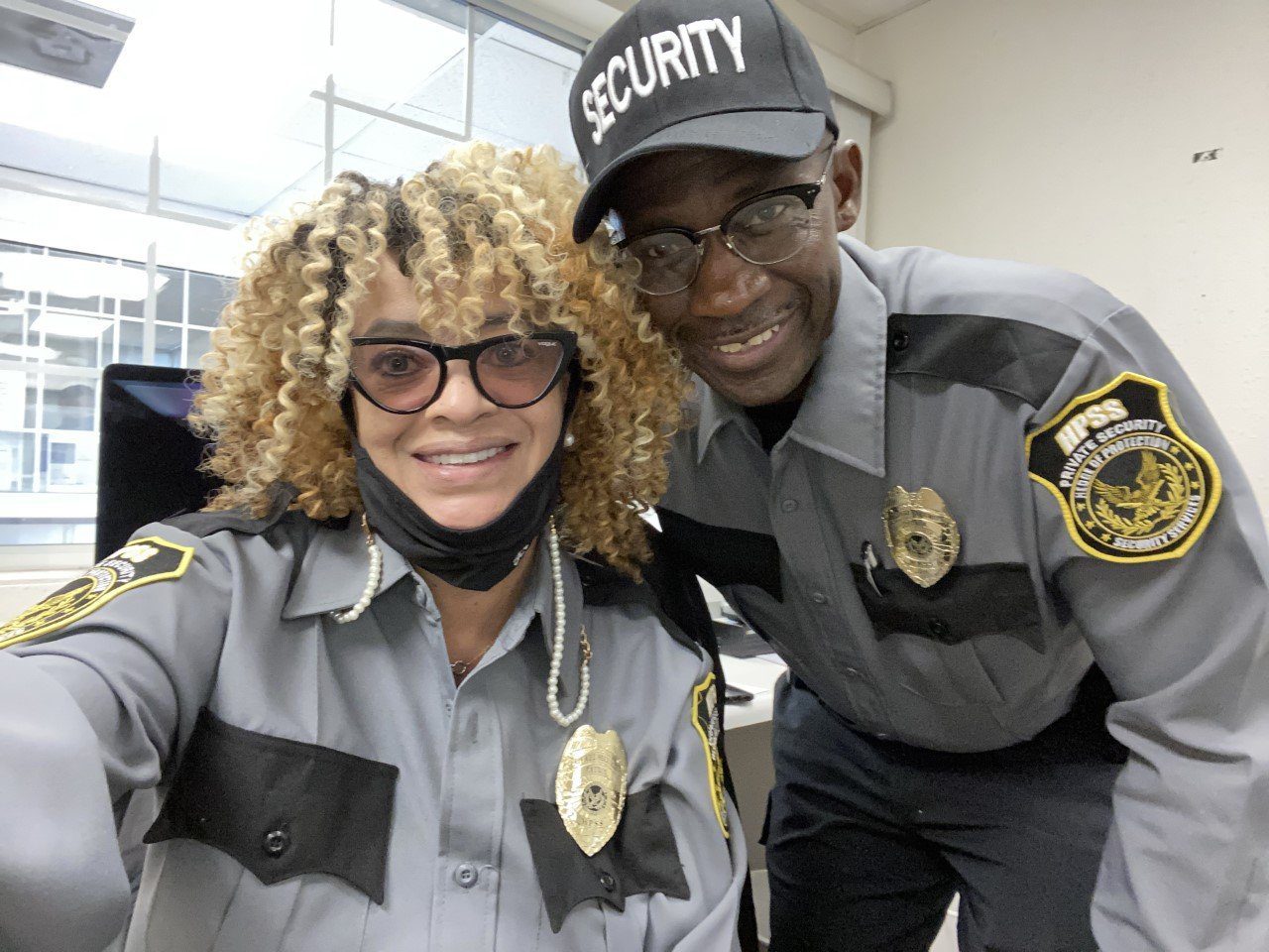 Two smiling security officers in gray uniforms pose for a selfie indoors.