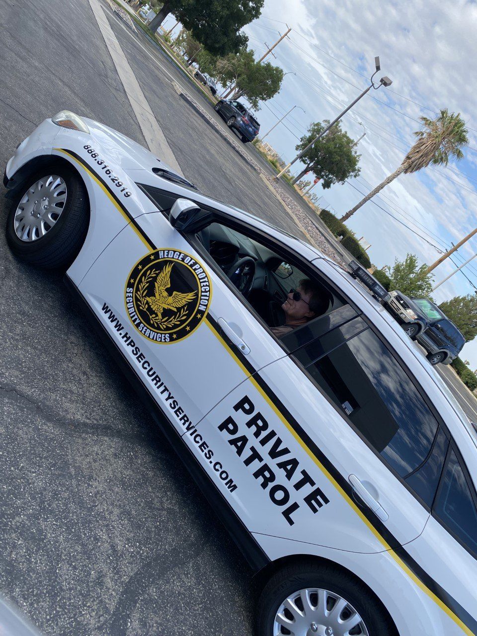 White private patrol car parked on a street, with black-and-gold logo and “PRIVATE PATROL” text on the side.