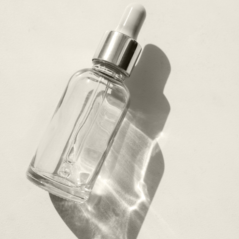 Clear glass dropper bottle with silver cap casting a shadow on a light background