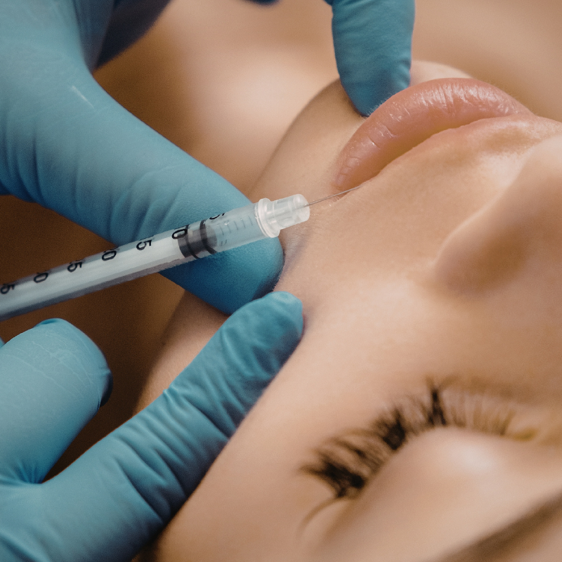 Gloved hands inject a syringe into a person’s cheek near the lips
