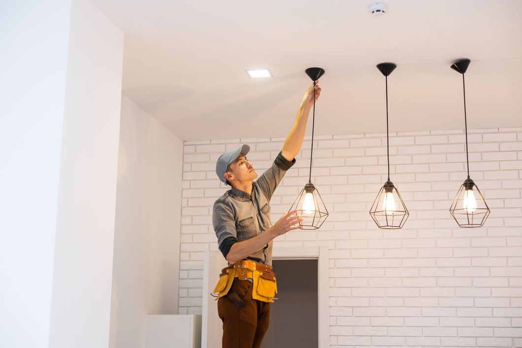 A person on a ladder installs a hanging light fixture in a room.