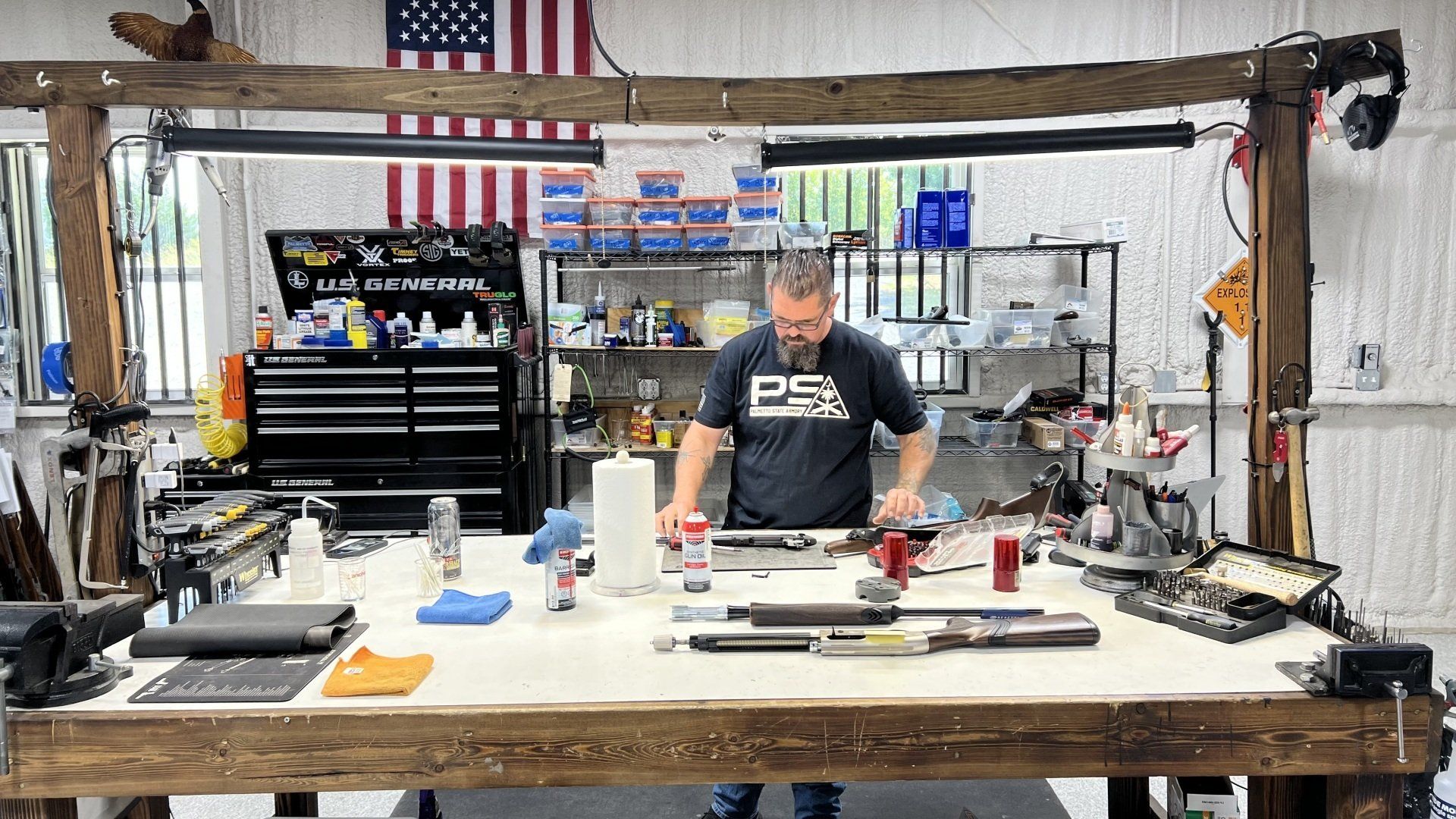 A man is standing at a wooden table in a workshop.