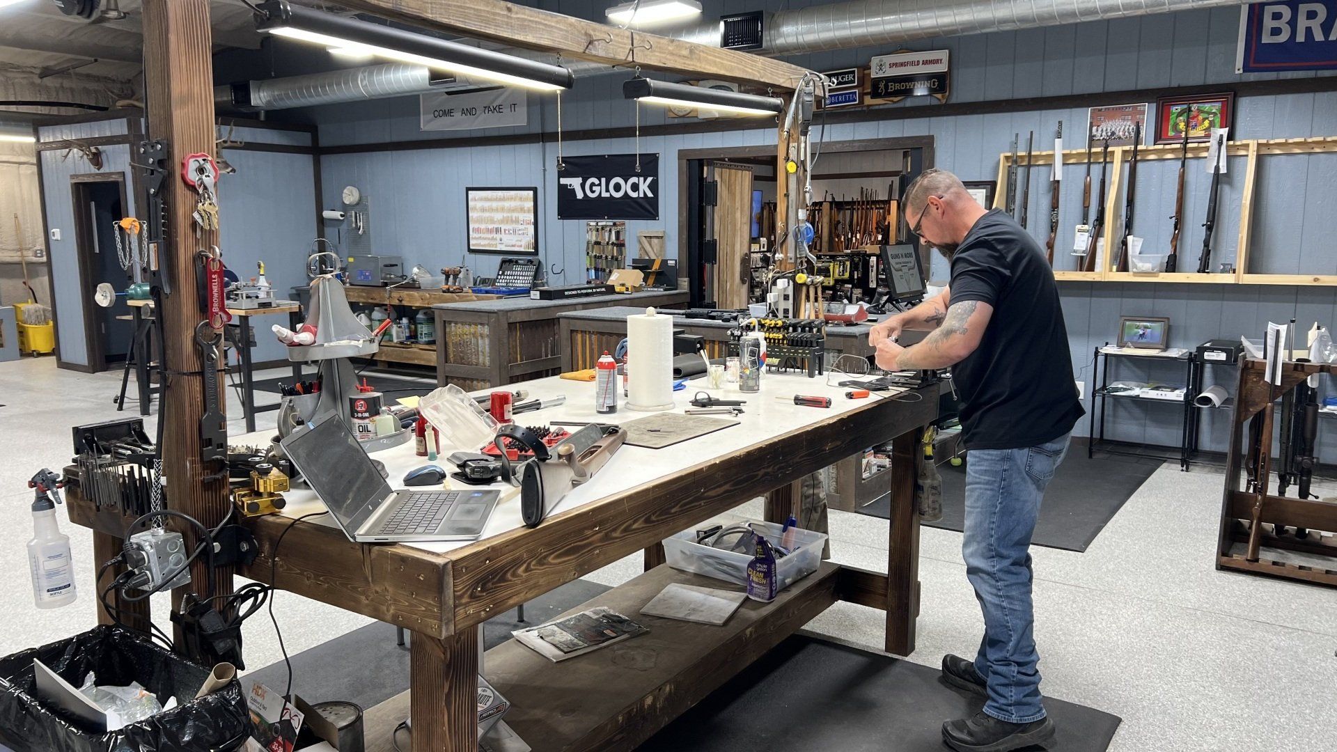 A man is standing in front of a wooden workbench in a workshop.