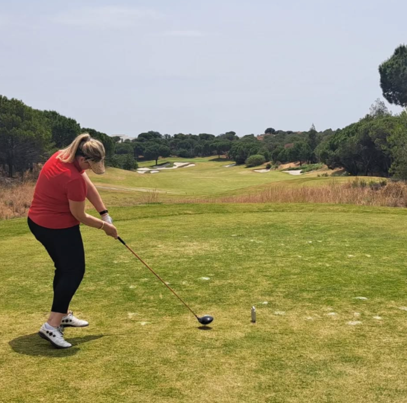 at dunas golf club Golfer in red shirt teeing off on a sunny golf course with trees lining the fairway