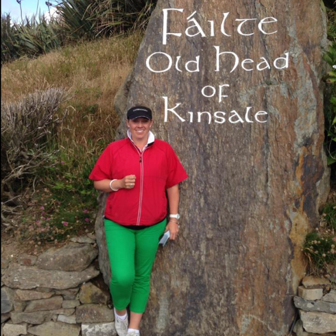 golfer in red shirt and green pants standing by a sign reading “Ealaíte Old Head of Kinsale”