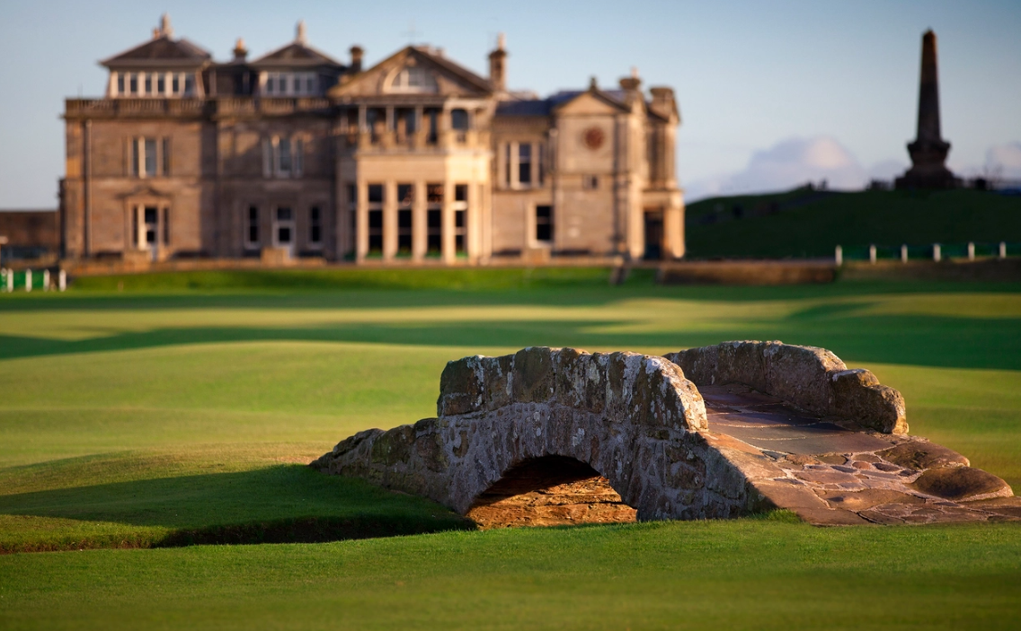 Golfer walking across the Swilcan Bridge on the Old Course at St Andrews with the town and clubhous