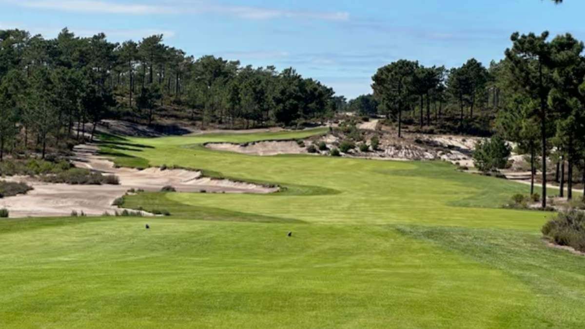 Green golf course fairway winding through rocky terrain with trees under a blue sky