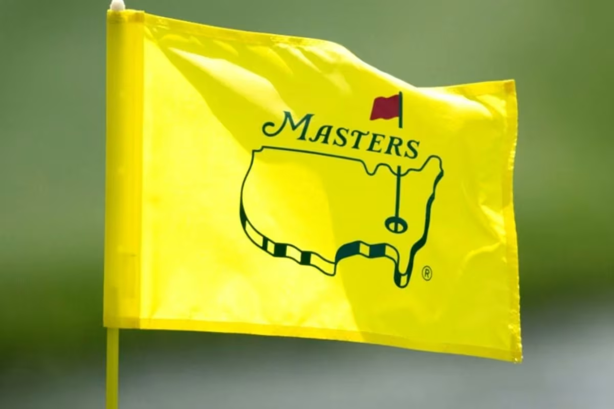 Yellow Masters golf flag with logo on a pole against a blurred green background