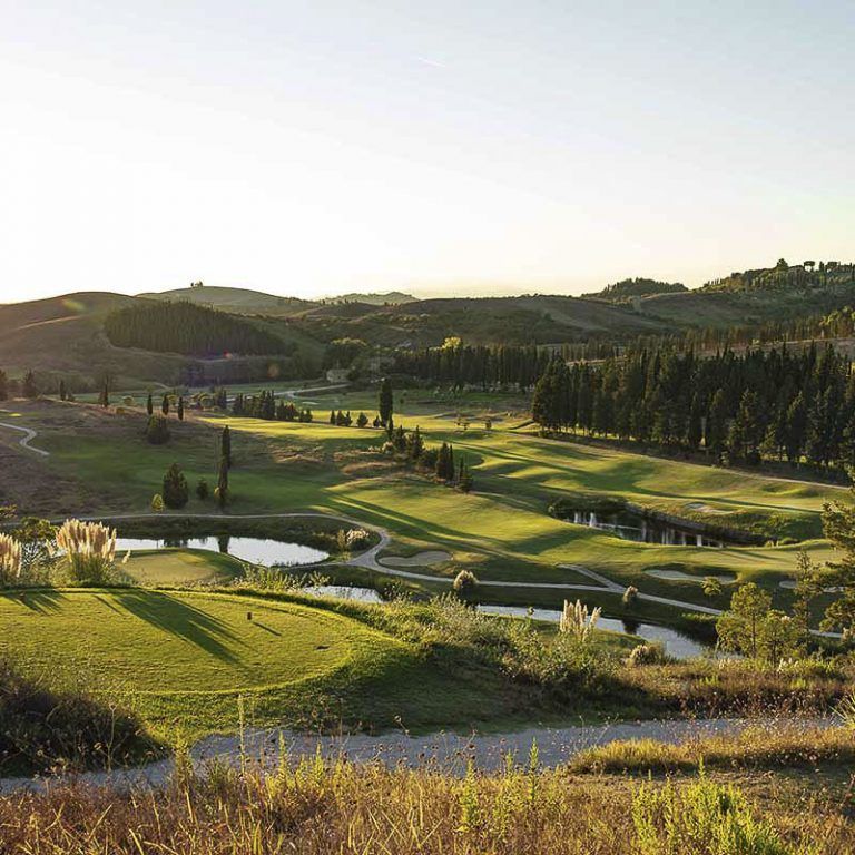 Sunlit golf course with green fairways, sand bunkers, and rolling hills at sunset