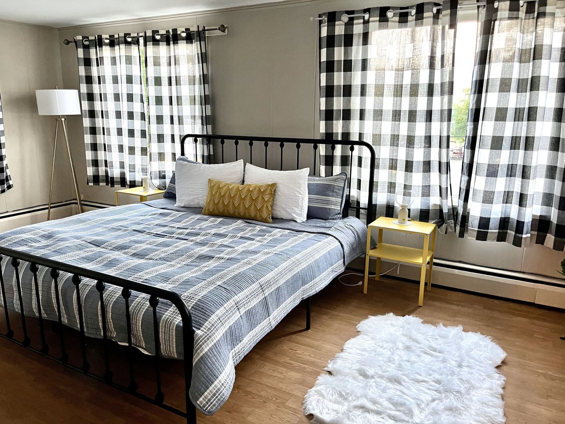 A bedroom with a king size bed , two nightstands , a rug , and black and white checkered curtains.