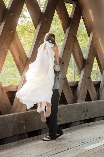 A man is carrying a bride in his arms on a wooden bridge.