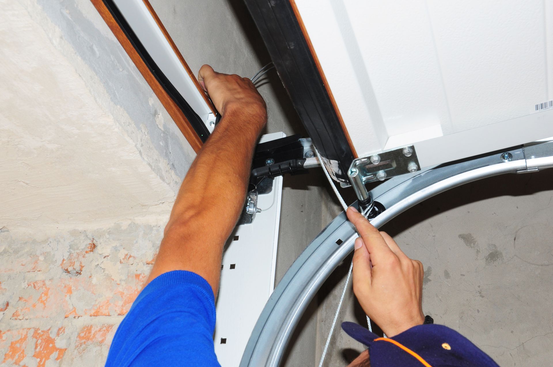 Hands installing a garage door track and opener on a ceiling-mounted rail.